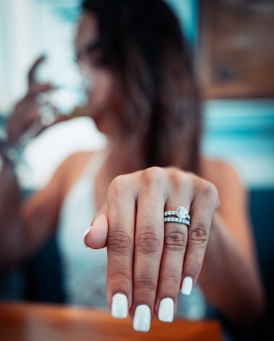 A young woman drinking from a stemmed glass and holding out a wedding ring